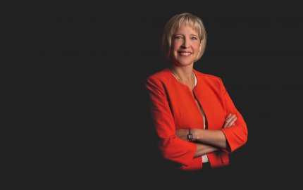 Holly Drumheller Butler is smiling, wearing a red jacket and beige top.