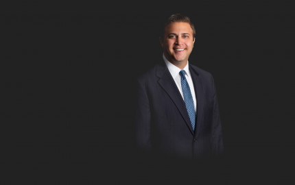 Joshua R Chazen is smiling, wearing a dark suit, white shirt, and blue tie with silver dots.
