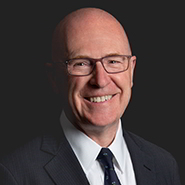 Stephen J. Cullen is smiling, wearing a dark suit, white shirt, and a blue tie. Close up on face.
