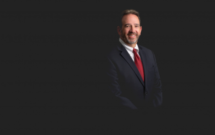 James W. Dawson Jr. is smiling, wearing a black suit, a white shirt with black pinstripes, and a red tie.