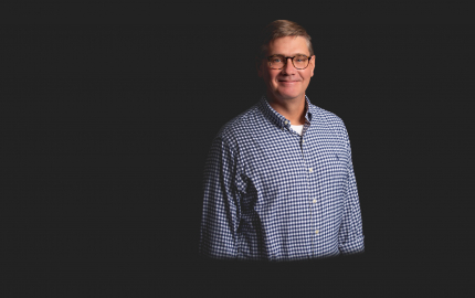 Joseph W. Hovermill is smiling, wearing a blue and white gingham shirt, with a white undershirt.