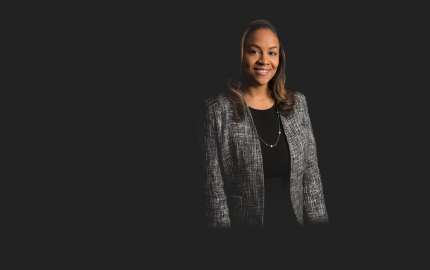 Veronica D. Jackson is smiling, wearing a grey jacket, and black dress.