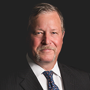 William M. Krulak, Jr. is smiling, wearing a black pinstripe suit, white shirt, and blue tie. Close up on face.