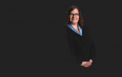 Meg E. Manchester is smiling, wearing a black jacket, and blue shirt.