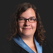 Meg E. Manchester is smiling, wearing a black jacket, and blue shirt. Close up on face.