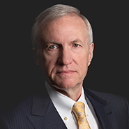 Raymond F. Monroe is wearing a dark pinstripe suit, white shirt, and yellow tie. Close up on face.