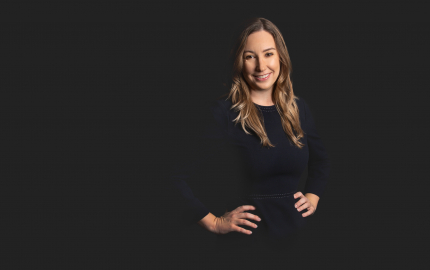 Kelly A. Powers is smiling and wearing a black dress with white stitching.