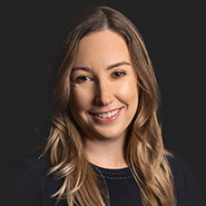 Kelly A. Powers is smiling and wearing a black dress with white stitching. Close up on face.