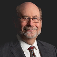 Russell V. Randle is smiling, wearing a grey suit, a white shirt, and grey and red tie. Close up on face.