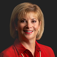 Suzanne L. Rotbert is smiling, wearing a red shirt, and dark pants. Close up on face.