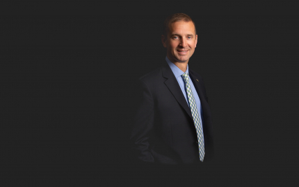 Jeremy S. Scholtes is smiling, wearing a dark suit, blue shirt, and blue and white striped tie.