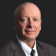 Rand D. Weinberg is wearing a black suit, white shirt, and black tie with brown stripes. Close up on face.