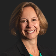 Kirsten M. Eriksson is smiling, wearing a black jacket, and green shirt. Close up on face.