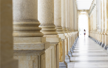 Two rows of stone columns forming a hallway with a person walking away.