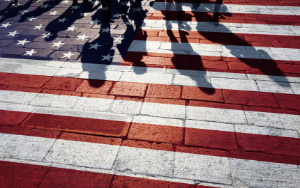 America flag painted on the sidewalk. Shadows of a group of people walking on the painting.