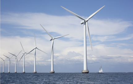 Large white windmills in the sea with a sailboat
