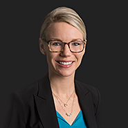 Leslie M. Cumber is smiling, wearing a black jacket, and a teal shirt. Close up on shirt.