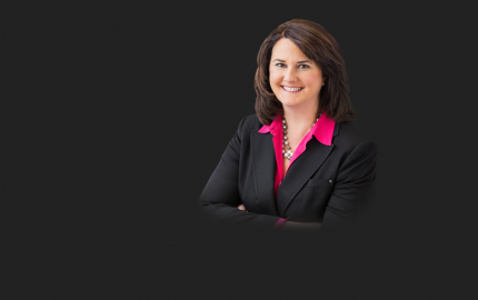 Suzzanne W. Decker is smiling, wearing a black jacket, and a pink shirt.