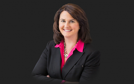 Suzzanne W. Decker is smiling, wearing a black jacket, and a pink shirt.