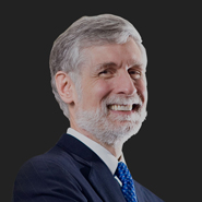 Thomas E. Zeno is smiling, wearing a blue suit, white shirt, and blue tie. Close up on face.