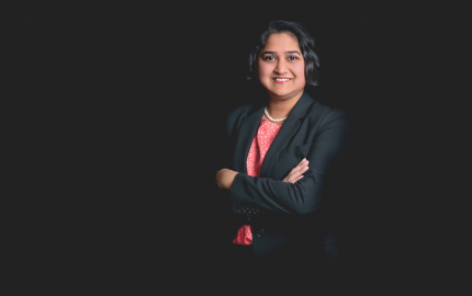 Tina R. Goel is smiling, wearing a black jacket, and a pink shirt with white flowers.
