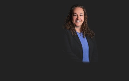 Stephanie K. Baron is smiling wearing a dark jacket with a blue shirt.