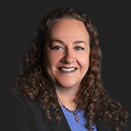Stephanie K. Baron is smiling wearing a dark jacket with a blue shirt. Close-up on face.