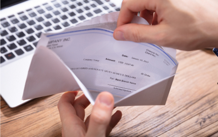Person removing a paycheck from an envelope with a laptop in the background.