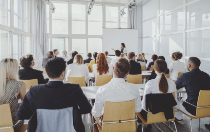 Woman standing in front of a crowded room appearing to give lesson