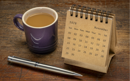 A full cup of coffee next to a small desktop calendar with a pen in the front