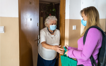 A young person delivering a bag to an elderly person at their door.