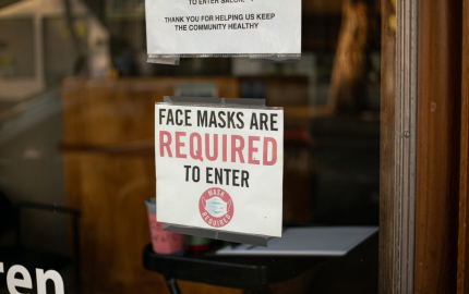 Paper sign taped to a window stating, Face Masks are Required to Enter