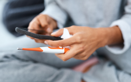 Person sitting down holding a cellphone, tissue, and thermometer in their hands