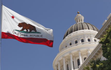 Dome on the California capitol building and the California state flag on a flag pole.