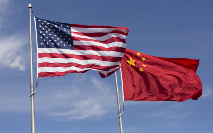 Chinese flag flying on a flagpole in the background and an American flag flying on a flagpole in the fore ground.