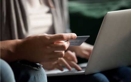 Person with an open laptop on their lap and another person holding up a credit card.