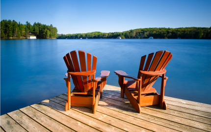 Empty Adirondack chairs on a wooden pier facing a lake,