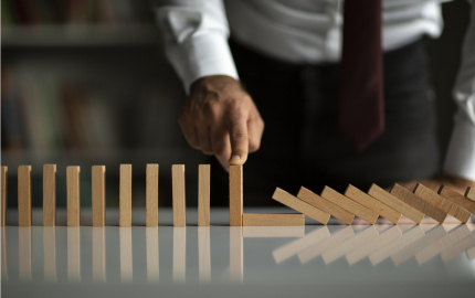 Person with their finger on top of a standing domino to prevent the dominos from falling.