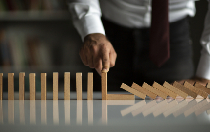 Person with their finger on top of a standing domino to prevent the dominos from falling.