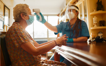 Medical Professional using infrared thermometer to take the temperature of a person sitting at a table.