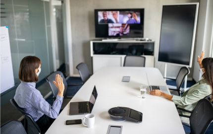 Two business professionals in a conference room having a teleconference with other people on a large monitor.