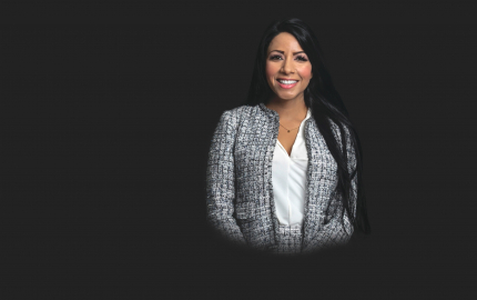 Sonia Shaikh is smiling, wearing a grey jacket, and white shirt.