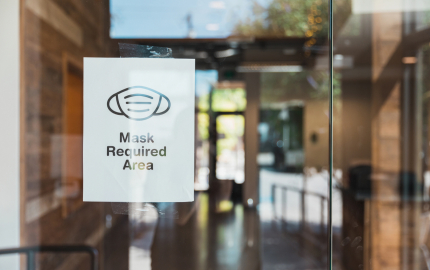 Paper sign taped in a window stating Mask Required Area