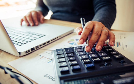 person sitting at a desk with one hand on a laptop and the other hand typing on a calculator.