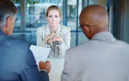 person sitting across the desk from two people who are looking at a piece of paper.