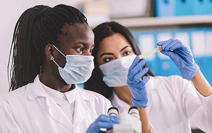 Two people in white lab coats and surgical masks looking at a vile.