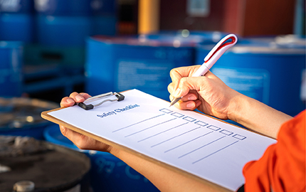 Person holding a clipboard with a blank safety checklist attached and a pen in the other hand preparing to write.