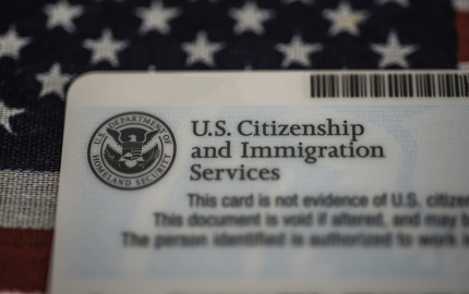 Top corner of the back of a Green Card with the U.S. Department of homeland security laying on top of an American flag.