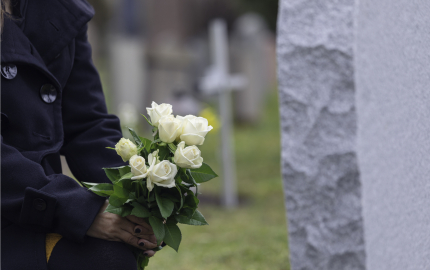 Person in a black pea coat holding a bouquet of white roses.