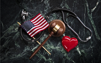 Stethoscpe with an American flag, a gavel on a sound block, and res heart, all on a marble background.